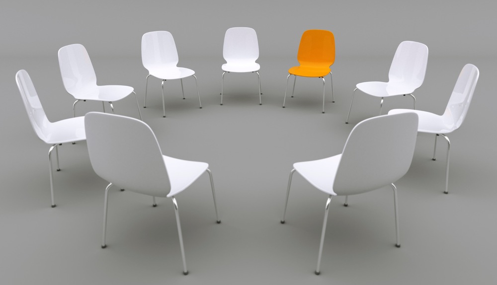 A circle of sleek modern chairs, all white except for one that is orange